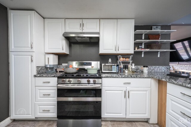 kitchen featuring under cabinet range hood, open shelves, dark stone countertops, white cabinetry, and stainless steel range with gas stovetop