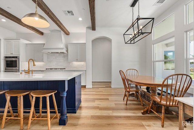 16711 Keystone Pl, Bakersfield, CA 93314 - kitchen with premium range hood, stainless steel oven, arched walkways, light wood-style flooring, and decorative backsplash
