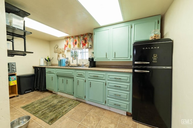 kitchen featuring black fridge, sink, light tile patterned flooring, and green cabinetry