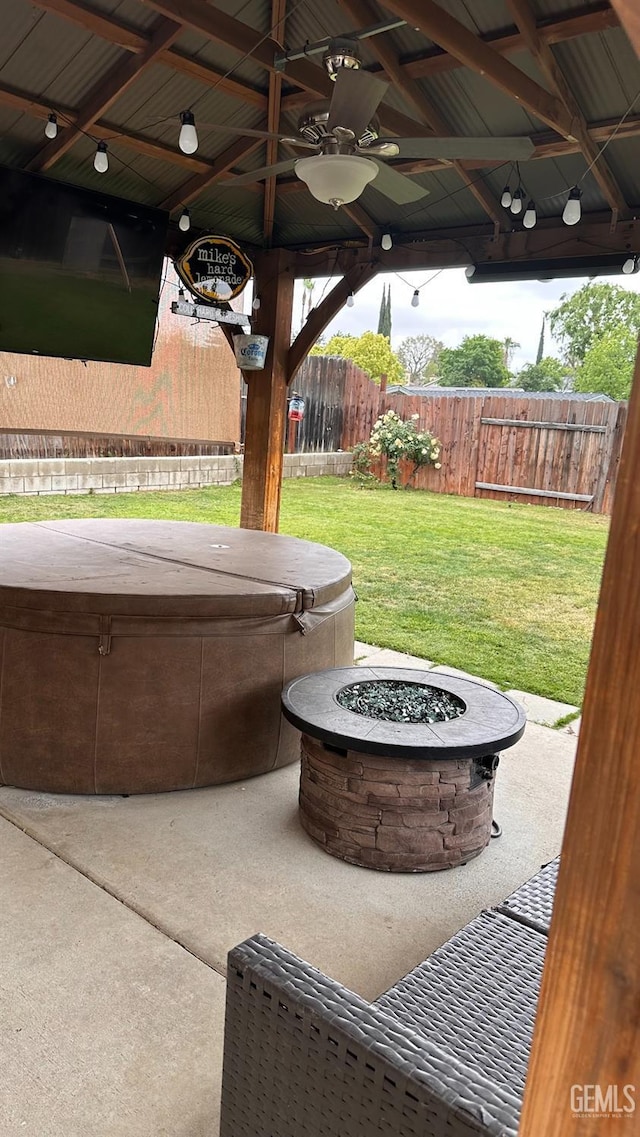 view of patio with fence, a hot tub, a ceiling fan, and an outdoor fire pit
