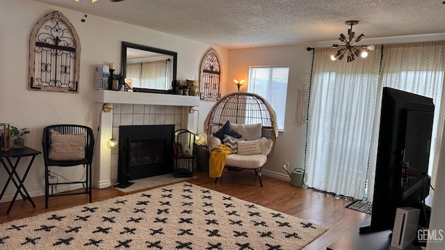 living area featuring wood finished floors, baseboards, a tiled fireplace, a textured ceiling, and ceiling fan with notable chandelier