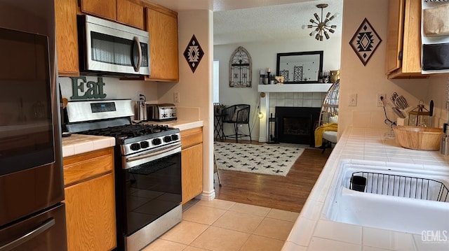 kitchen with tile countertops, open floor plan, light tile patterned floors, a fireplace, and appliances with stainless steel finishes