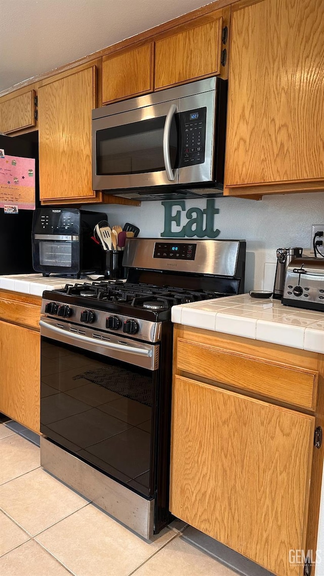 kitchen featuring light tile patterned floors, tile counters, brown cabinets, and appliances with stainless steel finishes