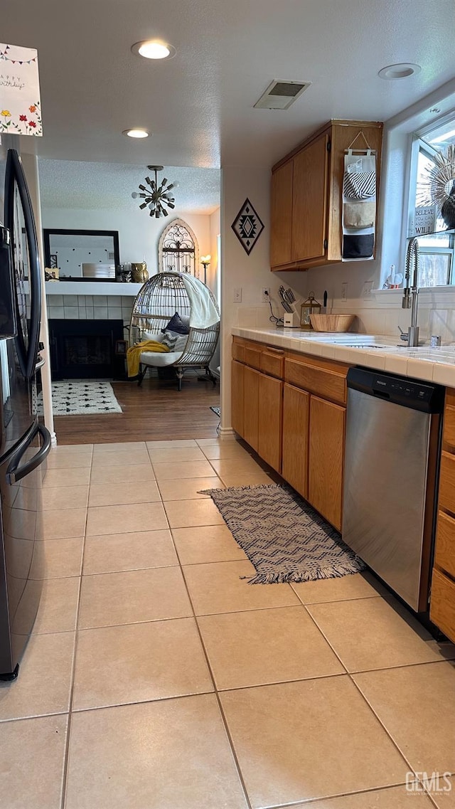 kitchen with stainless steel dishwasher, visible vents, black fridge with ice dispenser, tile counters, and light tile patterned floors