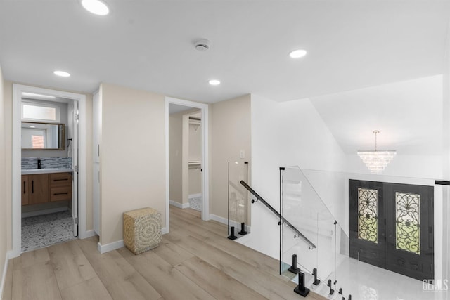 hall featuring an upstairs landing, light wood-type flooring, recessed lighting, and a notable chandelier