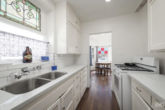 kitchen featuring dark wood-style floors, a sink, decorative backsplash, white cabinets, and white gas range