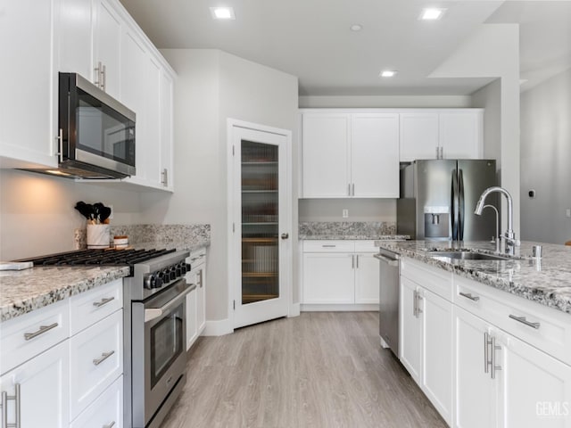 kitchen with stainless steel appliances, white cabinetry, and light stone counters