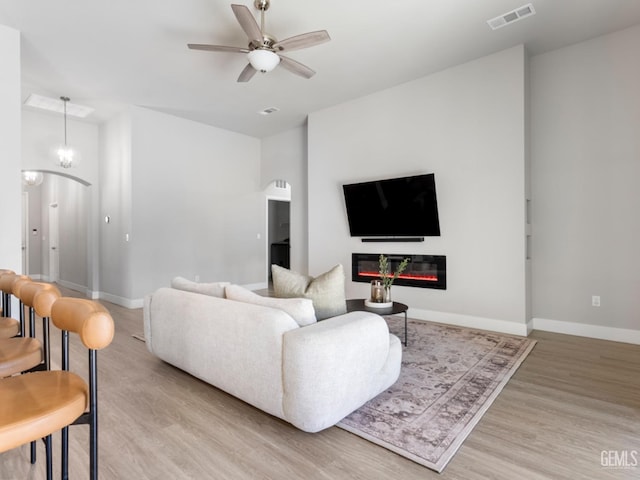 living room featuring baseboards, a glass covered fireplace, visible vents, and light wood-style floors