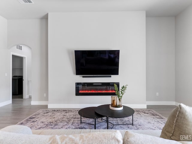 living room featuring wood finished floors, a glass covered fireplace, visible vents, and baseboards