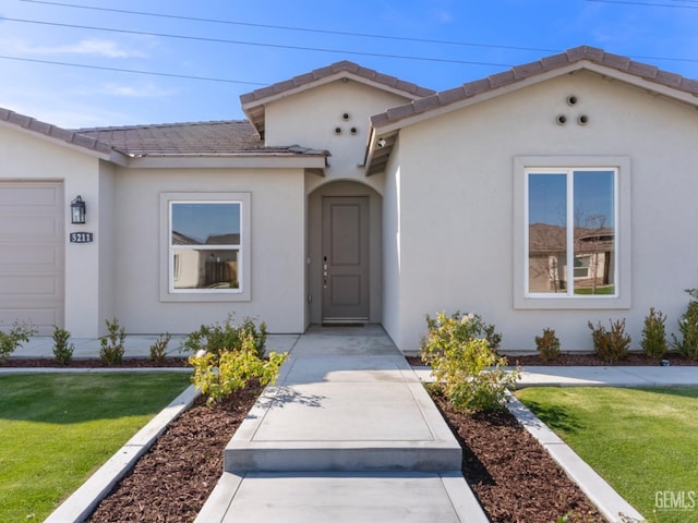 entrance to property with a tile roof, a lawn, and stucco siding