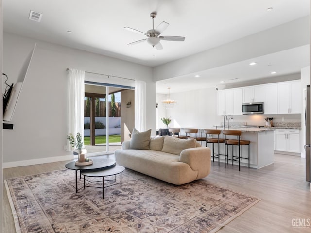 living area with light wood-style flooring, recessed lighting, ceiling fan with notable chandelier, visible vents, and baseboards