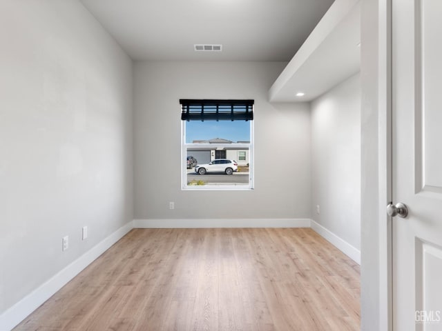 spare room featuring light wood finished floors, visible vents, and baseboards