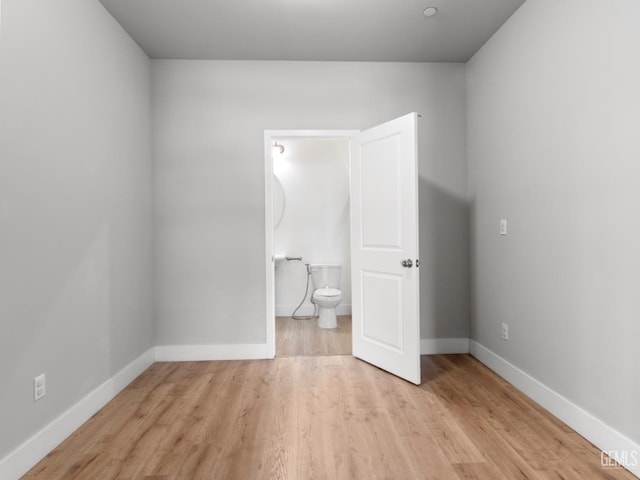 unfurnished bedroom with light wood-style floors, ensuite bath, and baseboards