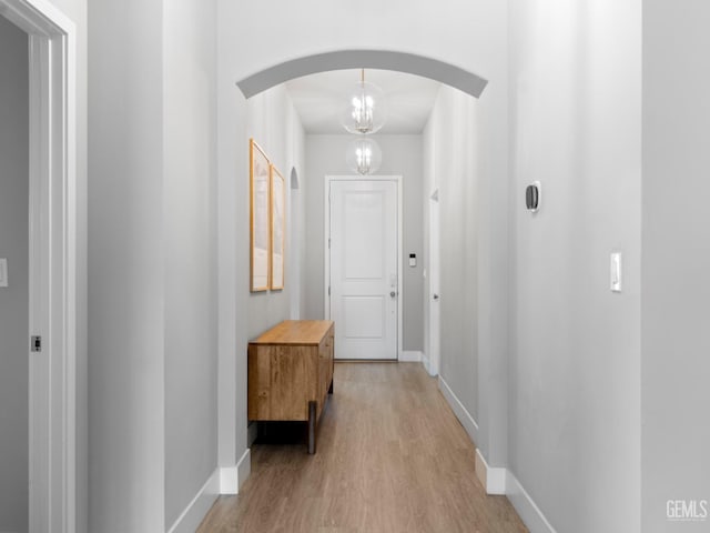 hallway with light wood finished floors, baseboards, and arched walkways