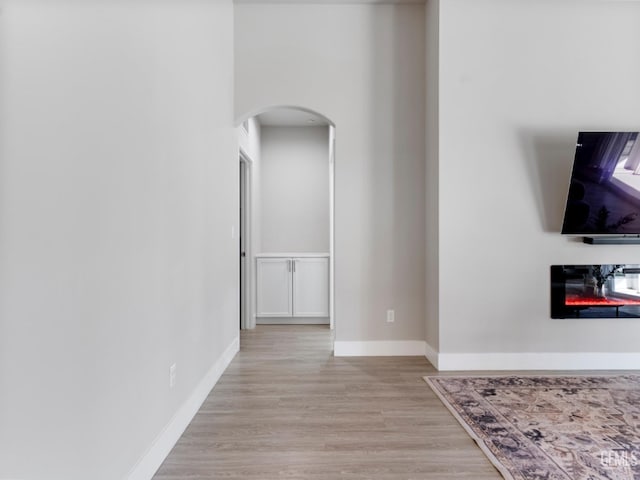 living area with light wood-type flooring, baseboards, arched walkways, and a glass covered fireplace