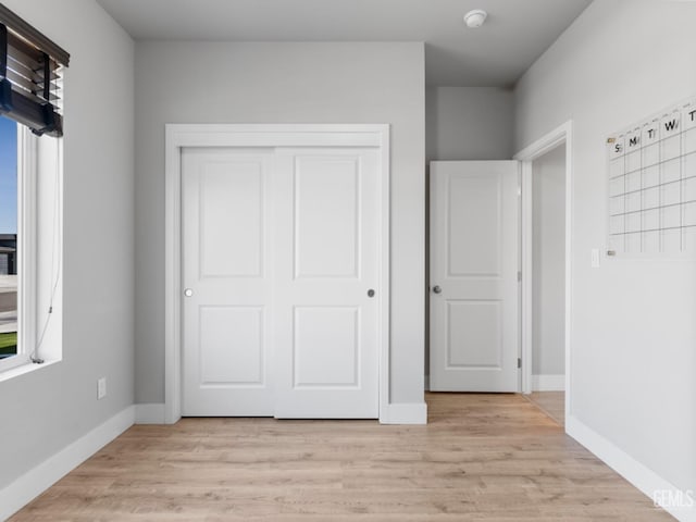 unfurnished bedroom featuring light wood-type flooring, multiple windows, and baseboards