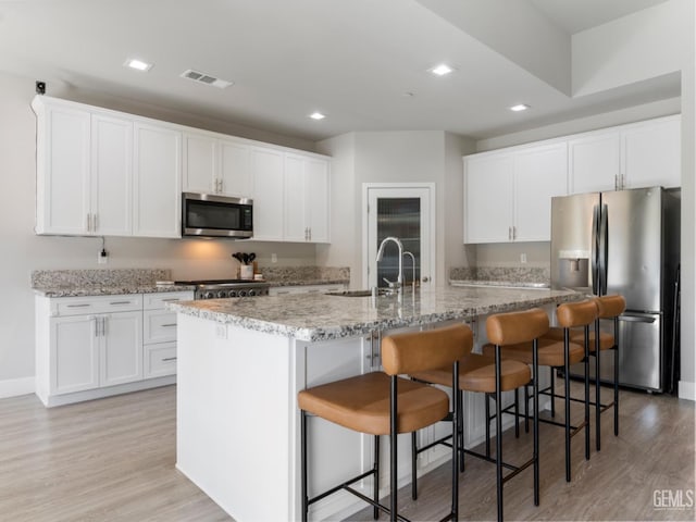 kitchen featuring stainless steel appliances, visible vents, a kitchen island with sink, white cabinets, and a sink