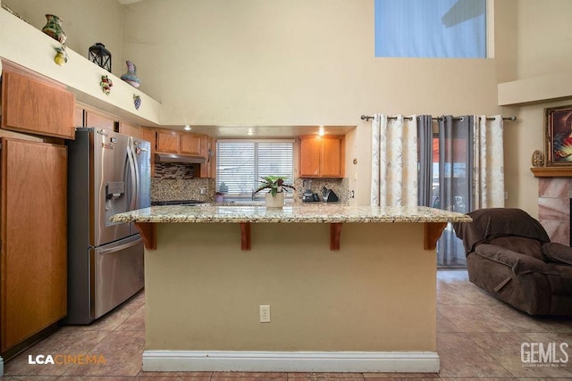 kitchen featuring light stone counters, stainless steel fridge, a towering ceiling, and a breakfast bar area