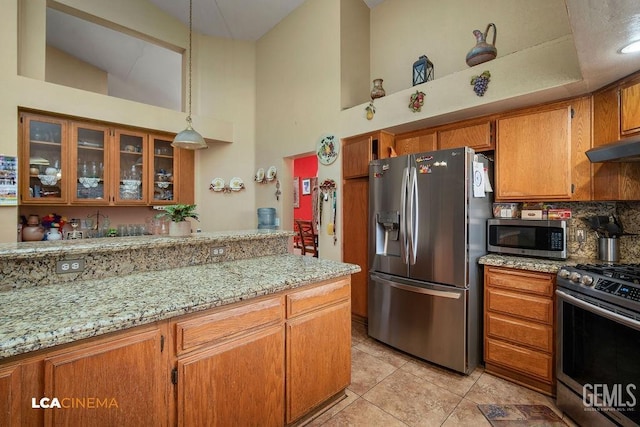 kitchen featuring light stone counters, pendant lighting, stainless steel appliances, light tile patterned floors, and high vaulted ceiling