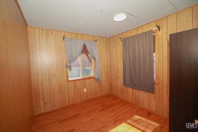 unfurnished room featuring wood-type flooring, a drop ceiling, and wooden walls