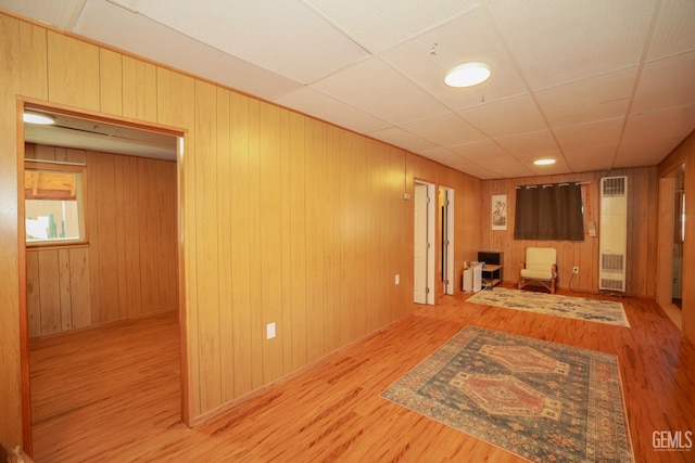 unfurnished living room with a paneled ceiling, wooden walls, and light hardwood / wood-style floors