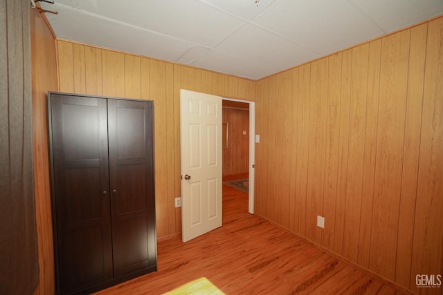 unfurnished bedroom featuring light hardwood / wood-style floors, wooden walls, and a closet