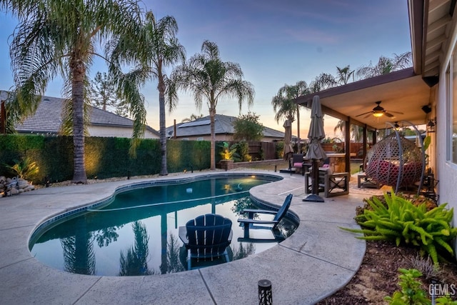 pool at dusk featuring ceiling fan and a patio area