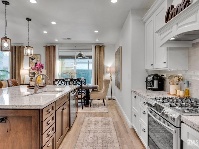 kitchen with sink, stainless steel appliances, light stone countertops, an island with sink, and white cabinets