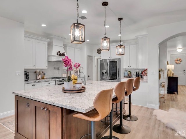 kitchen with pendant lighting, light hardwood / wood-style flooring, stainless steel appliances, white cabinets, and a center island with sink