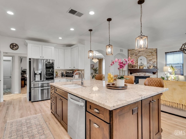 kitchen with pendant lighting, sink, appliances with stainless steel finishes, white cabinetry, and a center island with sink