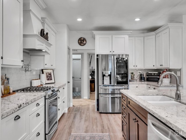 kitchen with stainless steel appliances, light stone countertops, sink, and white cabinets