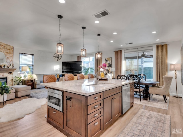 kitchen featuring appliances with stainless steel finishes, a stone fireplace, sink, a kitchen island with sink, and light hardwood / wood-style flooring