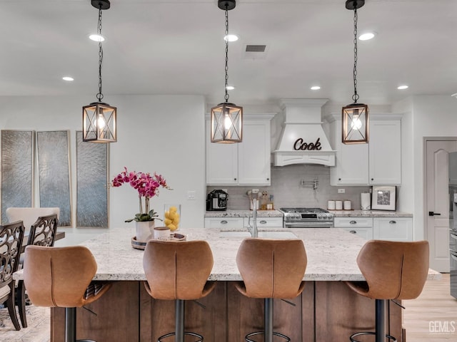 kitchen featuring white cabinetry, stainless steel stove, custom range hood, and pendant lighting