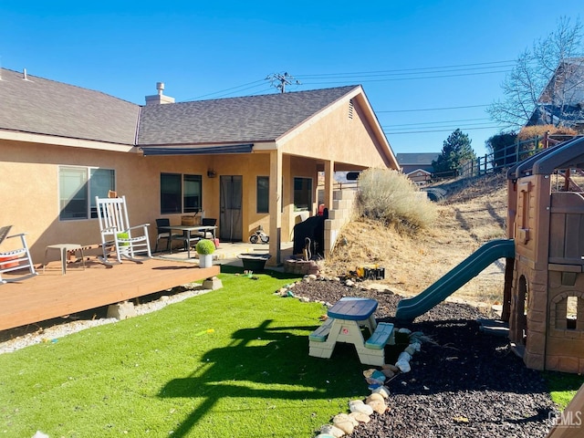 rear view of property with a deck, a yard, and a playground