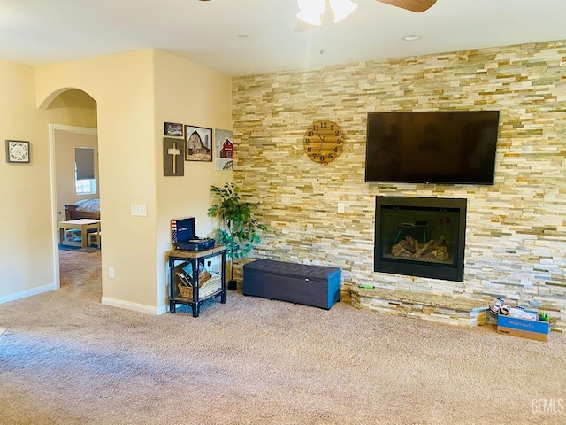 carpeted living room featuring ceiling fan and a stone fireplace