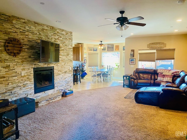 living room featuring ceiling fan, a stone fireplace, and carpet floors