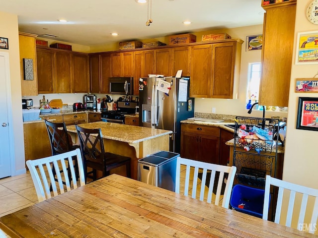 kitchen with light tile patterned floors, appliances with stainless steel finishes, a kitchen breakfast bar, light stone countertops, and a kitchen island