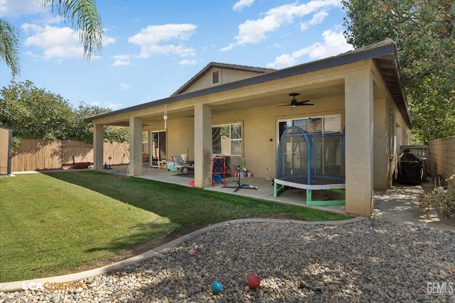 rear view of property featuring ceiling fan, a yard, a patio, and a trampoline