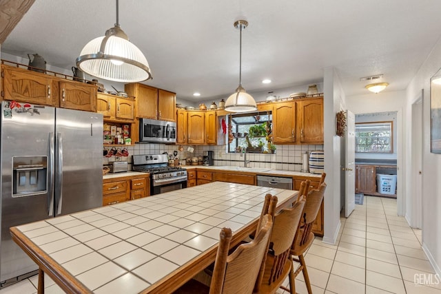 kitchen with sink, hanging light fixtures, decorative backsplash, appliances with stainless steel finishes, and tile counters