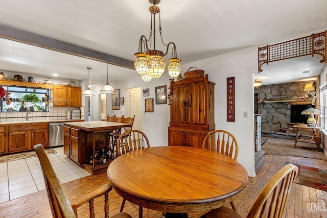 dining room featuring a chandelier, beam ceiling, light hardwood / wood-style floors, and a stone fireplace