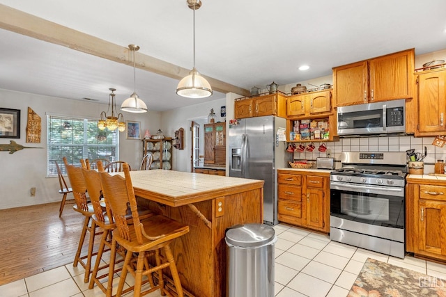 kitchen with a center island, light tile patterned floors, appliances with stainless steel finishes, tasteful backsplash, and decorative light fixtures