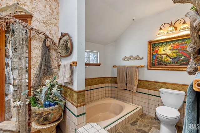 bathroom with tiled bath, toilet, tile walls, and lofted ceiling