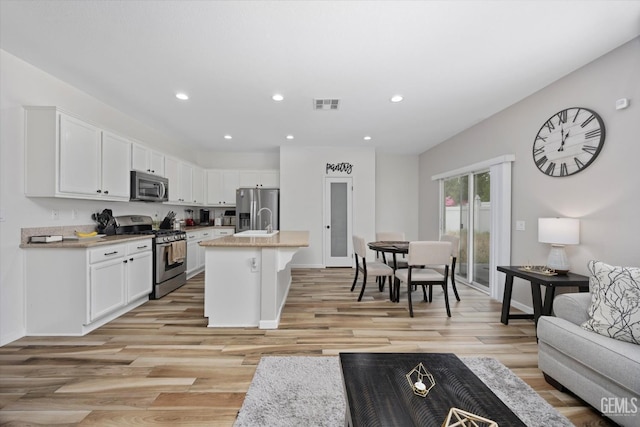 5711 Cordonata Way, Bakersfield, CA 93306 - kitchen with stainless steel appliances, white cabinetry, light wood finished floors, an island with sink, and a sink