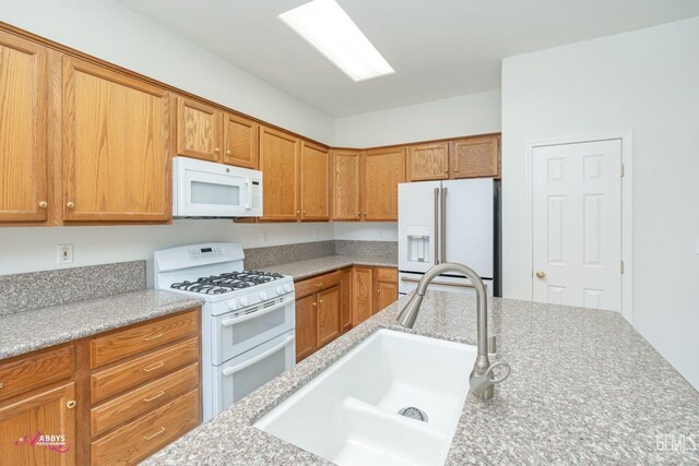 kitchen featuring light stone counters, sink, and white appliances