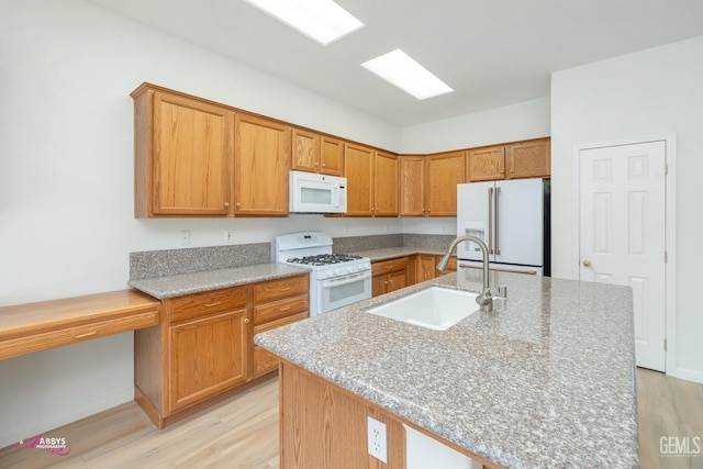 kitchen with light stone counters, sink, an island with sink, and white appliances