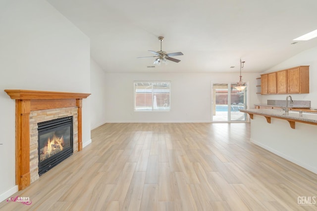 unfurnished living room with lofted ceiling, a stone fireplace, sink, ceiling fan, and light wood-type flooring