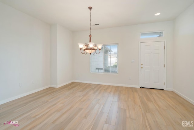 empty room with light wood-type flooring and an inviting chandelier