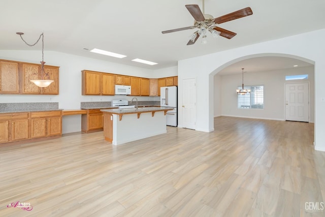 kitchen featuring a kitchen bar, a kitchen island with sink, hanging light fixtures, and white appliances