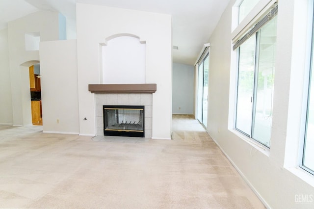 unfurnished living room with light carpet, vaulted ceiling, a wealth of natural light, and a tiled fireplace