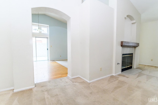 unfurnished living room with a tiled fireplace, light colored carpet, and lofted ceiling